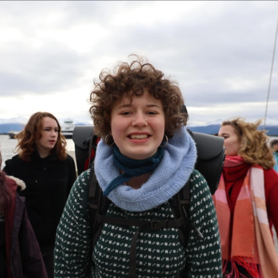 jente med sekk på ryggen står forran ungdommer og en ferje i vannet